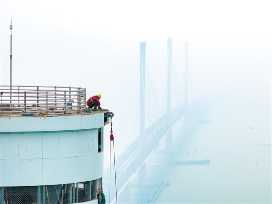 建設(shè)者在塔柱上施工，遠處“海上長龍”若隱若現(xiàn)。