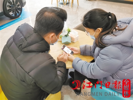 新能源汽車銷售人員協(xié)助車主用手機進行投保新能源汽車險。